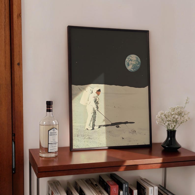 May include: A framed print of an astronaut playing golf on the moon. The astronaut is wearing a white spacesuit and is holding a golf club. The moon is in the background, and the Earth is visible in the sky.