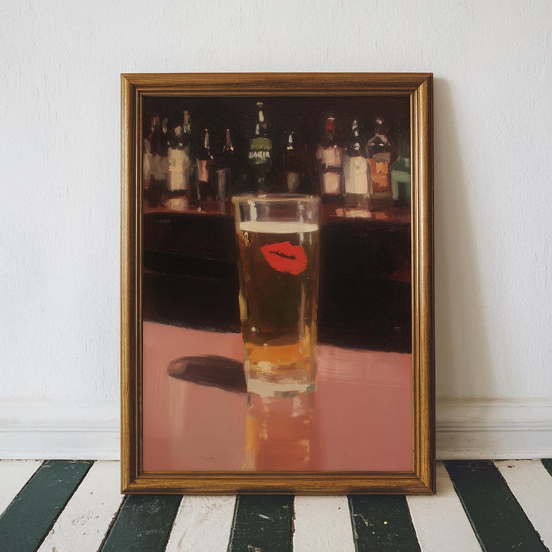 Puede incluir: Obra de arte enmarcada que presenta un vaso de cerveza con una huella de labios rojos. El vaso est&aacute; sobre una superficie rosa, con una barra y botellas en el fondo. El marco es de color dorado c&aacute;lido.