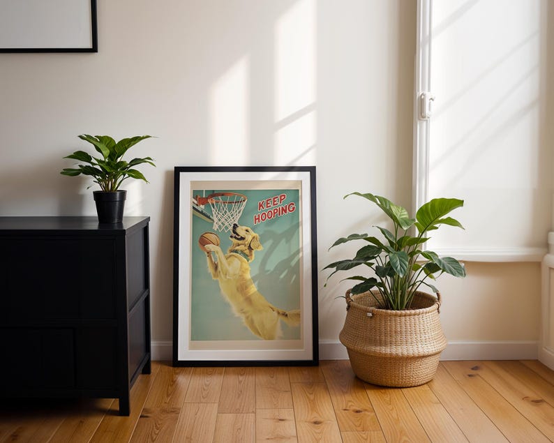 May include: A framed poster with a black border features a golden retriever dog dunking a basketball. The poster has the words "KEEP HOOPING" in red. The room has a black cabinet, a wicker basket with a plant, and a potted plant.
