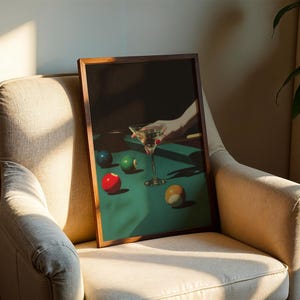 May include: A framed print featuring a still life of a martini glass and billiard balls on a green felt table. The artwork has a dark, moody aesthetic with a hand reaching for the glass. The balls are red, green, blue, and yellow.
