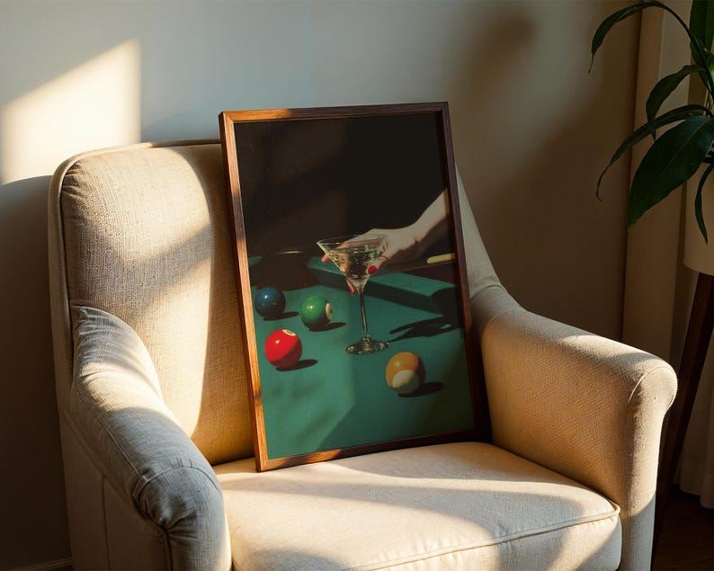 May include: A framed print featuring a still life of a martini glass and billiard balls on a green felt table. The artwork has a dark, moody aesthetic with a hand reaching for the glass. The balls are red, green, blue, and yellow.