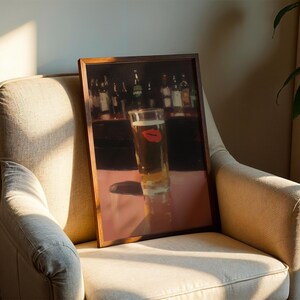 Puede incluir: Una impresi&oacute;n enmarcada de un vaso de cerveza con una huella de labio rojo, sobre un fondo de bar. La obra de arte se exhibe en un sill&oacute;n beige, con sombras de la luz solar.