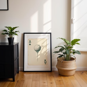 May include: A framed print of an ace of spades playing card with a golf ball on a tee in place of the spade symbol. The card is on a cream-colored background with black and green accents.