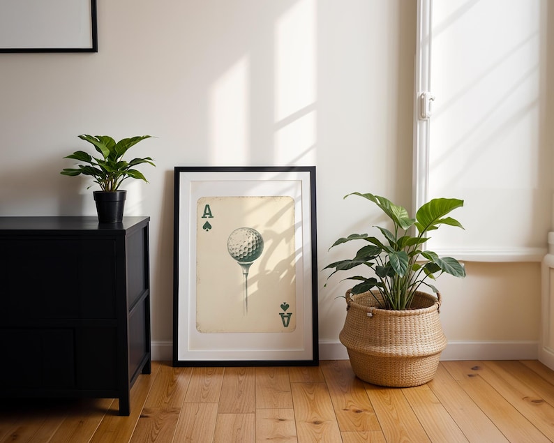 May include: A framed print of an ace of spades playing card with a golf ball on a tee in place of the spade symbol. The card is on a cream-colored background with black and green accents.