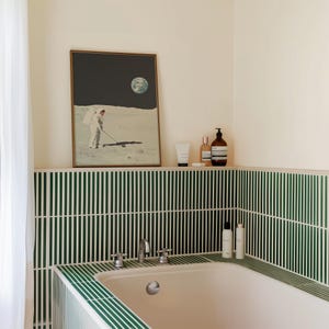 May include: A white bathtub with a green tiled surround. The tiles are arranged in a vertical pattern. There are bottles of toiletries on a shelf above the tub.