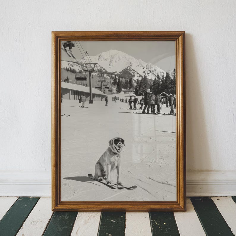 May include: Black and white framed print of a dog wearing ski goggles and skis, sitting on a snowy ski slope. The background shows a ski lift, skiers, and a mountain range. The frame is a warm brown color.