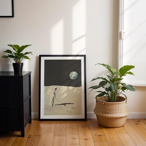 May include: A framed print of an astronaut playing golf on the moon with Earth in the background. The print is in a black frame and is hanging on a white wall.