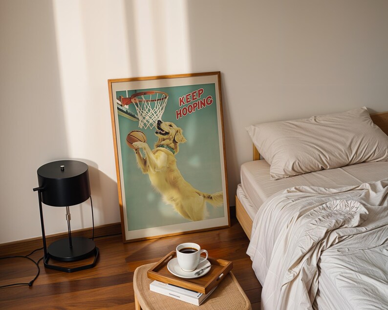 May include: A framed poster with a golden retriever dog playing basketball, with the words "KEEP HOOPING" in red. The poster is in a bedroom setting, with a bed, a side table, and a black lamp.
