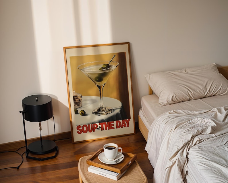 Peut inclure: Une affiche encadr&eacute;e avec un fond jaune et un verre &agrave; martini avec des olives. L'affiche dit "Soup of the Day" en lettres rouges. Une lampe noire avec un abat-jour rond est sur un sol en bois. Un lit avec une literie blanche est &agrave; l'arri&egrave;re-plan.