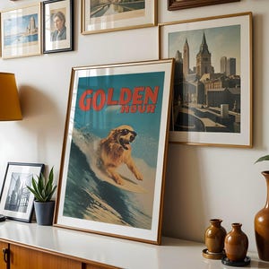 May include: A framed art print with a golden retriever surfing on a wave, wearing sunglasses. The print has the words "GOLDEN HOUR" in red. Other framed art pieces and a lamp are visible in the background.