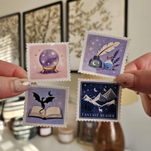 Puede incluir: Cuatro pegatinas cuadradas con ilustraciones de fantasía. Una presenta una bola de cristal, otra una pluma y tinta, una tercera un dragón y un libro, y la última una escena de montaña con el texto "FANTASY READER".