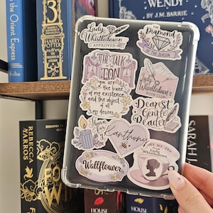 K&ouml;nnte beinhalten: Transparente Handyh&uuml;lle mit verschiedenen Aufklebern mit Texten und Illustrationen. Aufkleber enthalten S&auml;tze wie "Lady Whistledown Approved" und "Dearest Gentle Reader". Die H&uuml;lle wird in der N&auml;he eines B&uuml;cherregals mit B&uuml;chern gehalten.