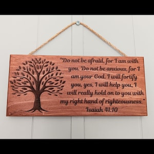 May include: A rectangular wooden sign with a tree design and the text "Do not be afraid, for I am with you...Isaiah 41:10". The sign is brown with a natural wood grain and is suspended by a natural fiber rope.