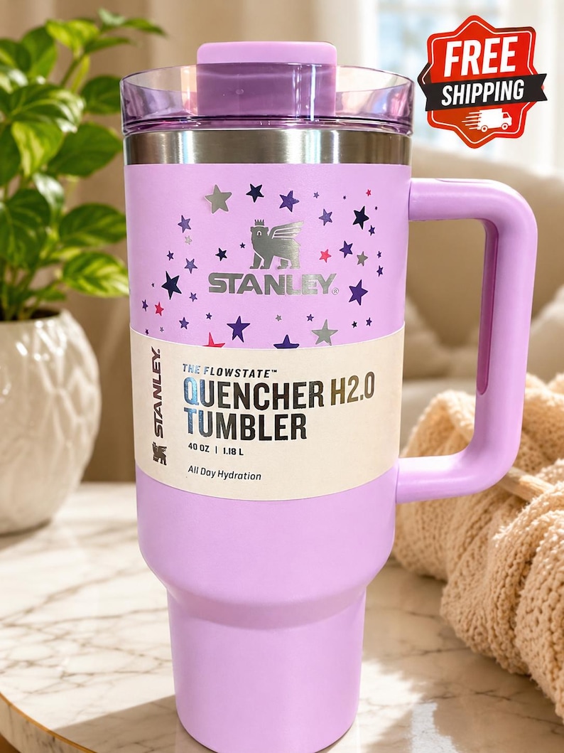 May include: A lavender Stanley Quencher H2.0 tumbler with a handle, lid, and star pattern. The tumbler holds 40 oz (1.18 L) and features the Stanley logo. The text "All Day Hydration" is printed on the label.