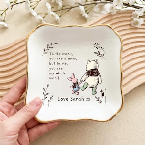 Może przedstawiać: Biała ceramiczna patera na biżuterię ze złotą obwódką, z ilustracją Kubusia Puchatka i Prosiaczka. Na paterze znajduje się napis "To the world, you are a mum, but to me, you are my whole world. Love Sarah xx."