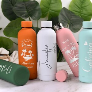 May include: A collection of insulated water bottles in various colors, including orange, white, pink, green, and light blue. Each bottle features personalized text and tropical-themed designs, ideal for a beach vacation or bridal party.