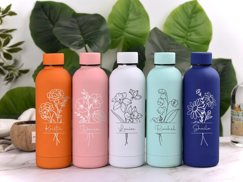 May include: Five colorful insulated water bottles. Each bottle is a different color: orange, pink, white, light blue, and dark blue. Each bottle has a floral design and a name etched on it. The bottles are displayed in front of large green leaves.