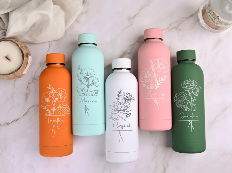 May include: Five colorful water bottles with floral designs and personalized names. The bottles are orange, light blue, white, pink, and green. Each bottle has a different flower design and name in a simple font.
