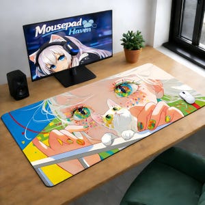 以下が含まれることがあります： カラフルなアニメスタイルのイラストが描かれた、大きな長方形のマウスパッド。鮮やかな目と白い猫の顔のクローズアップデザイン。マウスパッドには青、黄、緑のボーダーがあります。コンピューターモニターには「Mousepad Haven」というテキストが表示されています。