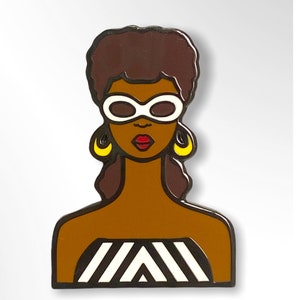 May include: A black and white striped pin with a brown-skinned woman wearing white sunglasses and yellow earrings. The woman has brown hair.