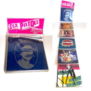 May include: A collection of Sex Pistols merchandise, including CDs and promotional items. The items feature the band's logo and album art, with a pink header that reads "Sex Pistols." One item displays the text "God Save the Queen."