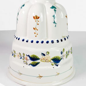 May include: White ceramic kitchenware with hand-painted floral designs in blue, green, and orange. The piece has a rounded top and a wider base, with a row of blue dots around the middle. Decorative and functional.