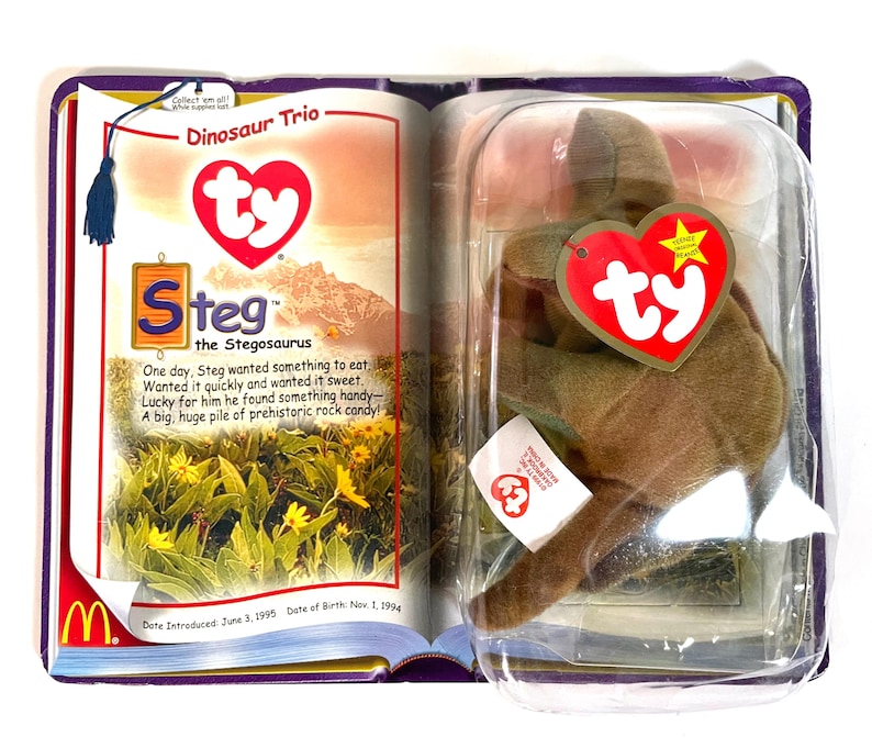Pu&ograve; includere: Un peluche Ty Beanie Baby Steg il Stegosauro, ancora nella sua confezione originale. La confezione include un libretto con il testo "Dinosaur Trio" e la storia di Steg. Il peluche &egrave; marrone e ha un'etichetta a forma di cuore rossa.