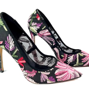 May include: A pair of black high-heeled shoes with floral embroidery in pink, purple, green, and red. The shoes have a pointed toe and a mesh panel. The heels are approximately 4 inches tall.
