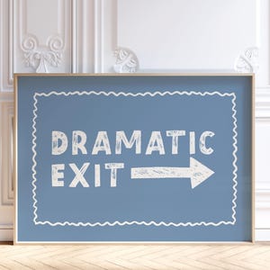 May include: A framed sign with the words "DRAMATIC EXIT" in white, with an arrow pointing right, on a blue background. The sign has a white, wavy border and a wooden frame. The sign is in a room with white walls and a wooden floor.