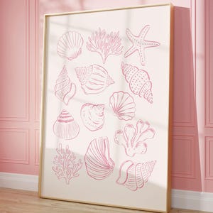 Może przedstawiać: Oprawiony wydruk z różowymi rysunkami liniowymi różnych muszli, koralowców i rozgwiazdy na kremowym tle. Grafika jest prezentowana na tle różowej ściany i drewnianej podłogi, tworząc motyw nadmorski.