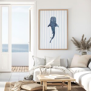 May include: A framed art print featuring a watercolor illustration of a whale shark. The artwork is in shades of blue and white, with a striped background. The print is displayed in a light-colored wooden frame.