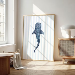 May include: A framed art print featuring a watercolor illustration of a whale shark. The artwork is in shades of blue and white, with a striped background. The frame is gold, and the print is displayed in a well-lit room.