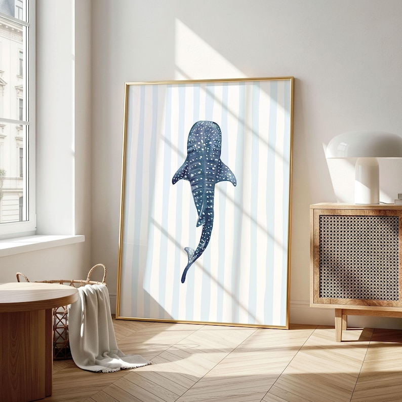 May include: A framed art print featuring a watercolor illustration of a whale shark. The artwork is in shades of blue and white, with a striped background. The frame is gold, and the print is displayed in a well-lit room.