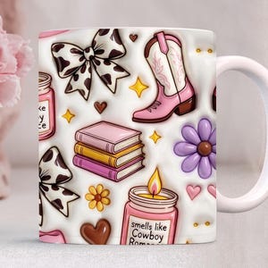 May include: White ceramic mug featuring a repeating pattern of pink cowboy boots, cow print bows, books, flowers, hearts, and candles. The candle jar reads "smells like Cowboy Romance".