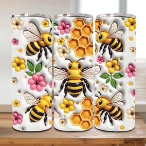 May include: A set of three stainless steel tumblers with a white background, featuring a repeating pattern of yellow and black bees, honeycomb, and colorful flowers. The design is 3D-like with raised elements.