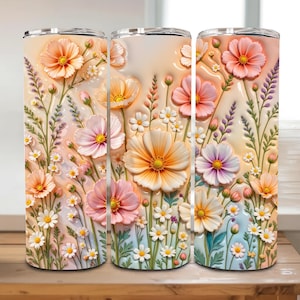 May include: Three stainless steel insulated tumblers with a floral design. The design features embossed flowers in shades of peach, pink, and white, with green stems and leaves. The background is a gradient of light peach and blue.