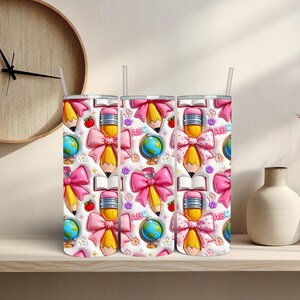May include: Three white insulated tumblers with a repeating pattern of school-themed illustrations. The pattern includes yellow pencils with pink bows, globes, open books, red apples, and the letters "ABC" on a white background. Each tumbler has a white straw.