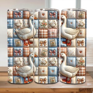 May include: A cylindrical tumbler featuring a patchwork quilt pattern with white geese, pink bows, hearts, floral squares, blue gingham, and small rectangular signs labeled Garden Seeds. The design repeats across the surface in a grid layout.