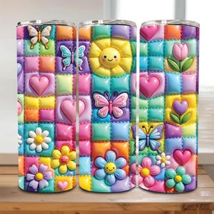 May include: A cylindrical tumbler featuring a colorful, quilted-style pattern of raised squares. The design includes pastel-colored hearts, smiling suns, various flowers, and butterflies in shades of pink, yellow, blue, orange, and purple.