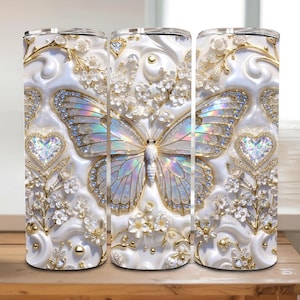 May include: A set of three white insulated tumblers with a butterfly design. The butterfly has iridescent wings and is surrounded by floral and heart-shaped accents. Gold and crystal embellishments add a touch of elegance to the design.