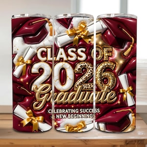 Op de afbeelding: Een tumbler met een afstudeerthema. Het ontwerp toont de tekst "Class of 2026 Graduate" in goud, afstudeerhoeden, diploma's en gouden linten. De achtergrond is dieprood met een glanzende afwerking.