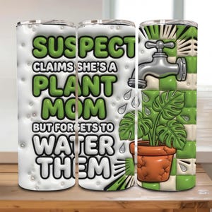 Op de afbeelding: Een witte beker met een humoristisch ontwerp. De tekst luidt "SUSPECT CLAIMS SHE'S A PLANT MOM BUT FORGETS TO WATER THEM" in groen en wit. Het ontwerp omvat een kraan, waterdruppels en een plant in een pot.