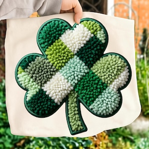 Può includere: Una borsa tote color crema con un grande design a trifoglio strutturato. Il trifoglio è realizzato con varie tonalità di verde e bianco, creando un effetto dimensionale. Il design è delineato da un bordo verde scuro.
