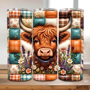 May include: A cylindrical tumbler featuring a patchwork quilt design with a central Highland cow illustration. The pattern includes orange, teal, and brown squares with floral and plaid motifs, accented by lavender and daisy floral arrangements.
