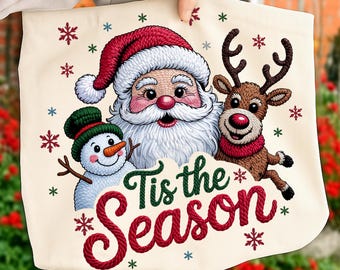 May include: A cream-colored tote bag featuring a festive holiday design. Santa Claus, a snowman, and a reindeer are depicted, along with the phrase "Tis the Season" in red and green. Snowflakes are scattered around the characters.