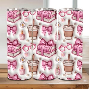 Op de afbeelding: Een witte tumbler met een herhalend patroon van roze boeken met strikken, brillen, koffiebekers, kaarsen en bloemen. Het ontwerp is cartoonachtig, met een 3D-effect. De tumbler is ontworpen voor koude dranken.