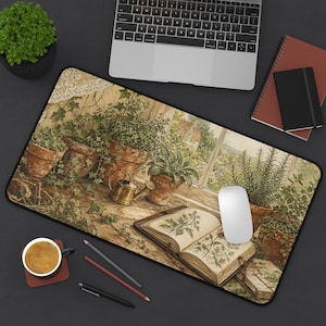 May include: A rectangular desk mat featuring a printed illustration of terracotta pots with green plants, a small brass watering can, and an open botanical book with detailed plant sketches. The mat has a black border and a smooth surface texture.