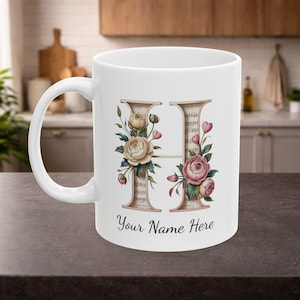 Puede incluir: Taza de cerámica blanca con un diseño floral de la letra "H" y el texto "Your Name Here". La letra está adornada con rosas crema y rosas, hojas verdes y notas musicales. Un artículo de cocina decorativo.