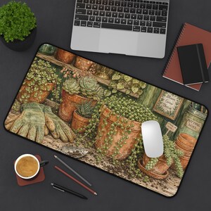May include: A rectangular desk mat featuring a printed illustration of a potting bench with terracotta pots, succulents, a string of pearls plant, and gardening gloves. The mat includes text labels reading Bloom Grow Thrive, String of Pearls, and Potting Soil.
