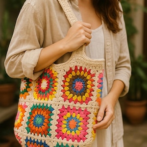 May include: A beige crochet tote bag with a colorful floral pattern. The bag features a series of square, multi-colored floral designs in shades of pink, orange, yellow, blue, and green. The bag is held by a person.